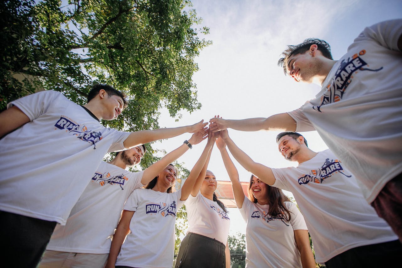 about-us A group of young adults in white shirts sharing a joyful team moment outdoors.